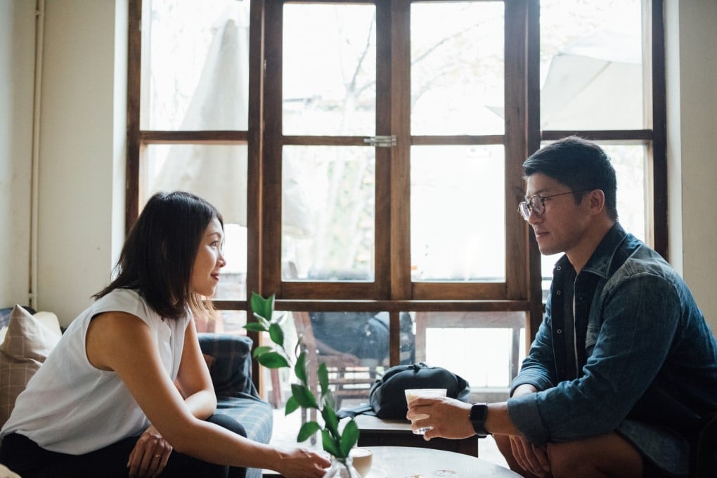 Medium shot of young Asian couple drinking coffee, sitting against the window, relaxing at cafe.