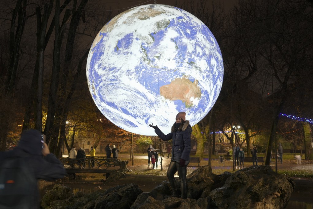 A girl poses by a depiction of the Earth at a light installation by British artist Luke Jerram in Bucharest on Saturday. Romania recently relaxed some of its pandemic restrictions. Photo: AP