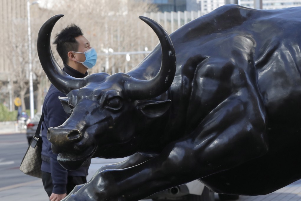 A man wearing a mask walks by a bronze sculpture of a bull in Beijing’s central business district. Photo: EPA-EFE
