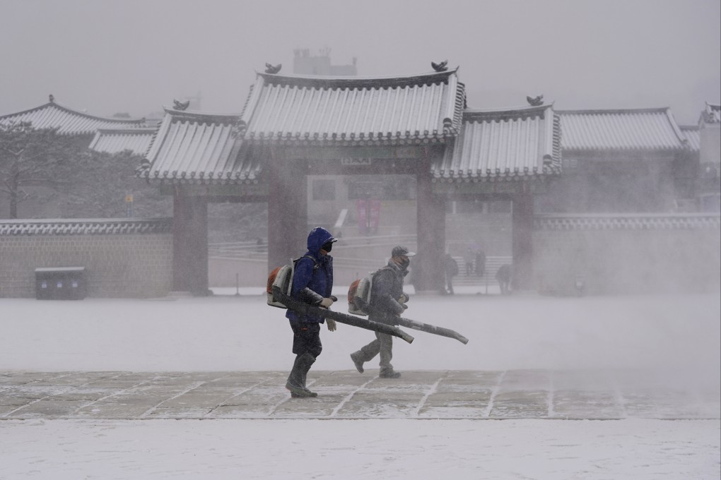Workers wearing face masks to help curb the spread of Covid-19 clear snow at the Gyeongbok Palace in Seoul, South Korea. Photo: AP