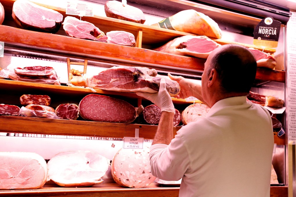 A grocer holds a piece of prosciutto ham in a deli. Photo: Reuters