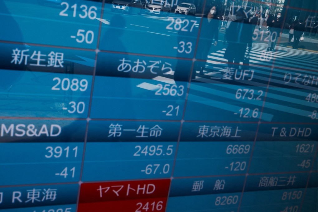 Passersby wearing protective face masks are reflected on a stock quotation board in Tokyo on January 25. A new book argues that the problems exposed by Covid-19 are inextricably linked, and stem from our reliance on unfettered financial market capitalism. Photo: Reuters