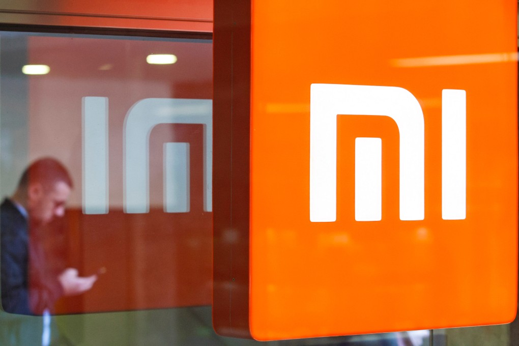 A man looks on his a mobile phone as he stands next to a reflected Xiaomi logo outside a store selling the smarphone brand in Kyiv on October 22, 2018.