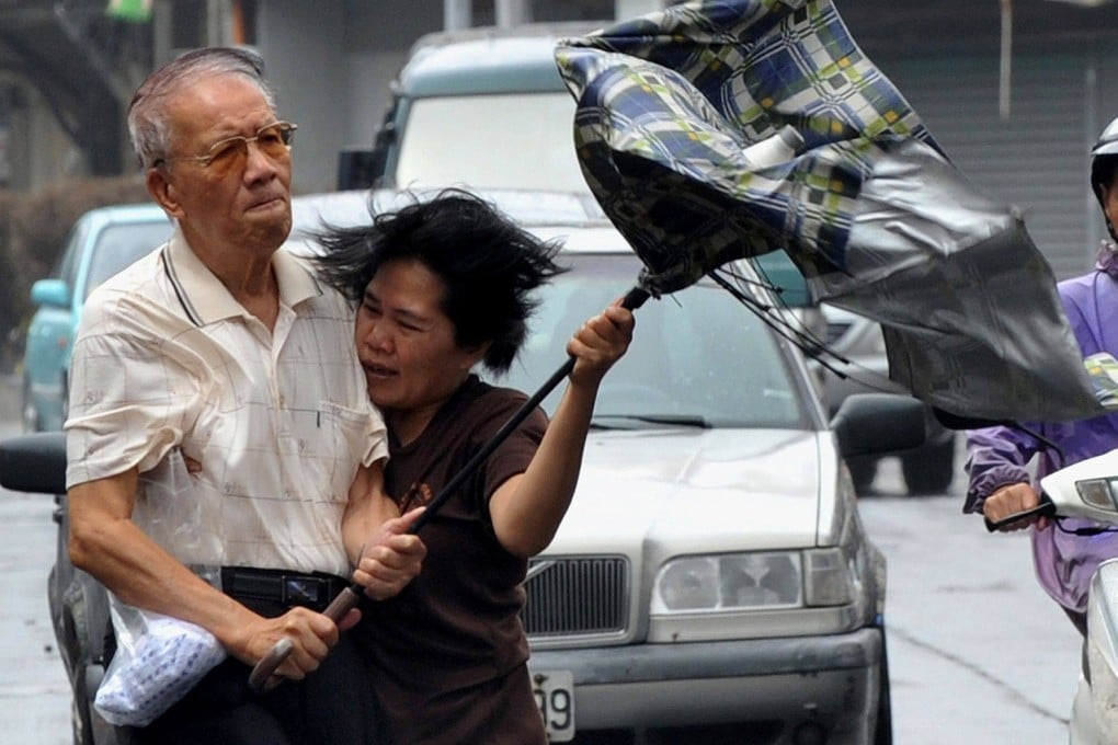 An elderly man, assisted by a foreign domestic helper, holds a wind-blown umbrella while walking on a windy street. Photo: AFP