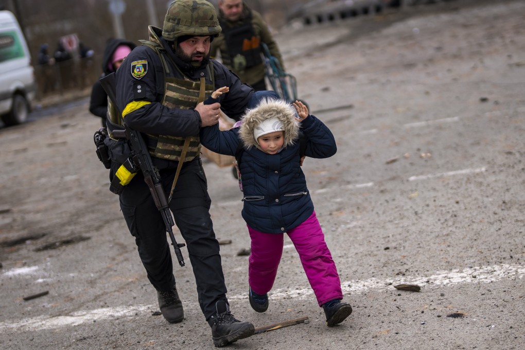 A Ukrainian police officer runs with a child as the artillery echoes nearby, while fleeing Irpin on the outskirts of Kyiv, Ukraine, on Monday. Photo: AP