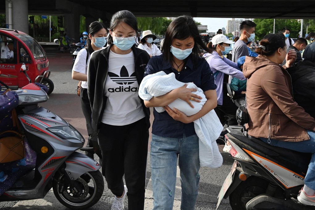 A woman carries a baby through a busy intersection in Beijing on June 2, 2021, days after China announced it would allow couples to have three children. Photo: AFP