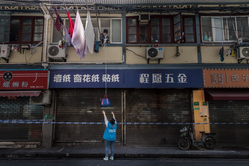 A quarantined man lowers a bag on a rope to a woman standing on the street in Shanghai,  March 29, 2022. Photo: EPA-EFE