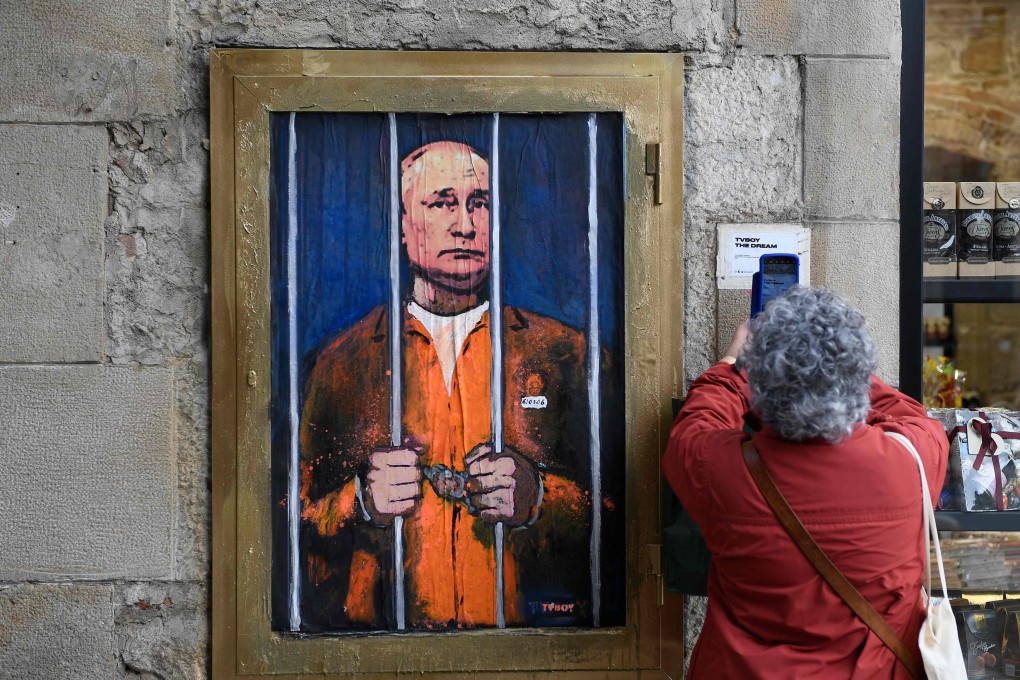 A woman in Barcelona on Thursday takes a picture of a painting by Italian street artist TvBoy depicting Russian President Vladimir Putin handcuffed and behind bars. Photo: AFP