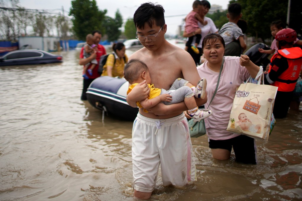 A man holding a baby wades through a flooded road following heavy rainfall in Zhengzhou, Henan province, on July 22, 2021. The Chinese province suffered US$19 billion worth of economic losses from the floods. Photo: Reuters