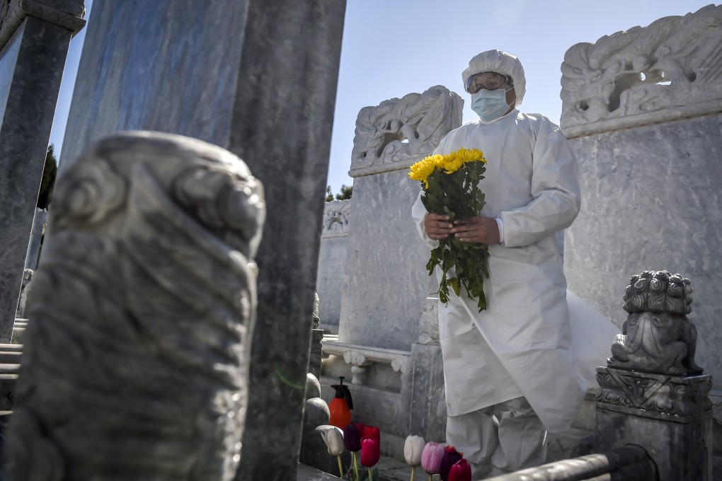 A cemetery worker in a protective suit makes an offering at a grave site in Beijing. Photo: AP