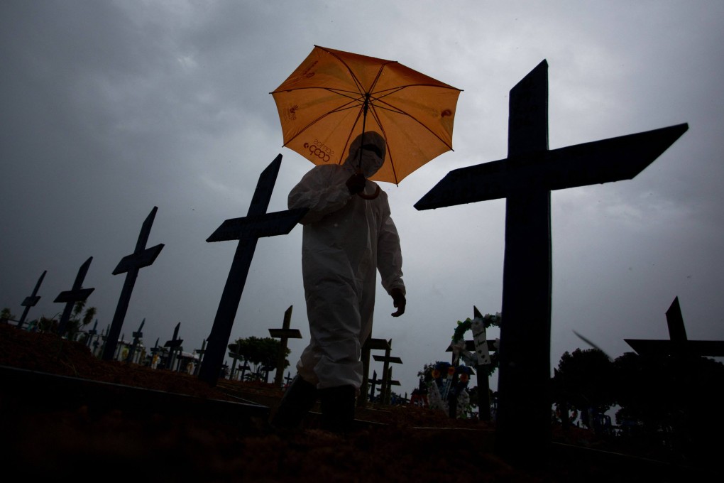 A worker wearing a protective suit and carrying an umbrella walks past the graves of Covid-19 victims at a cemetery in Manaus, Brazil in February 2021. Photo: AFP