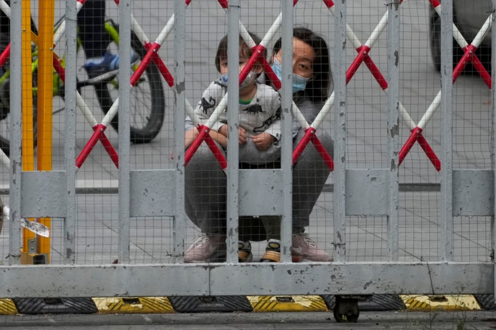A resident and a child look out through gaps in the barriers at a closed residential area during lockdown in Shanghai on May 10, 2022. Photo: Reuters.
