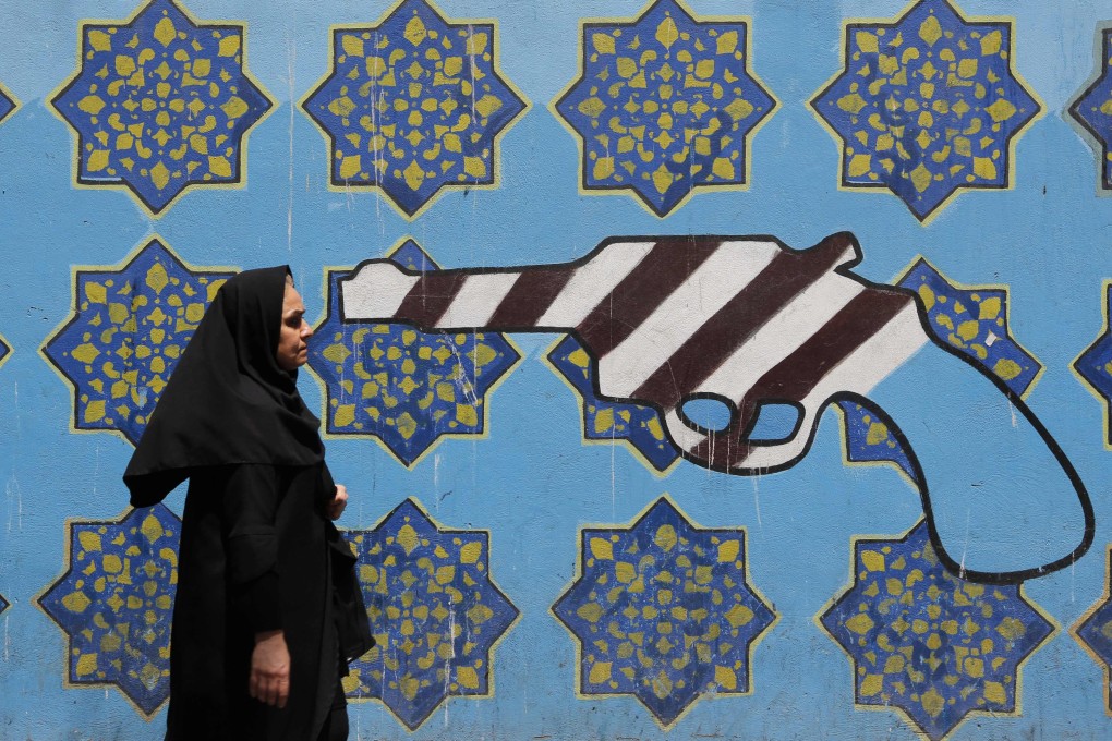 TOPSHOT - An Iranian woman walks by a mural painting on the wall of the former US embassy in the Iranian capital Tehran on August 7, 2018 US President Donald Trump warned countries against doing business with Iran today as he hailed the “most biting sanctions ever imposed”, triggering a mix of anger, fear and defiance in Tehran. / AFP PHOTO / ATTA KENARE