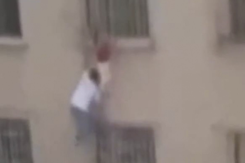 Man climbs six floors up the outside of a building to save a girl who became trapped hanging from security bars after falling from a window. Photo: Weibo