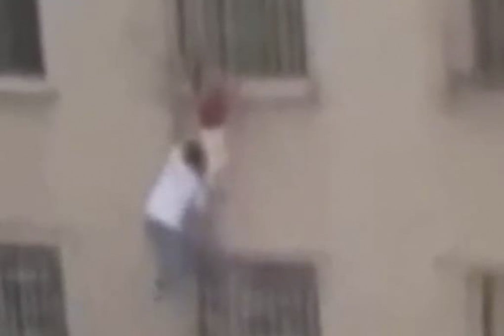 Man climbs six floors up the outside of a building to save a girl who became trapped hanging from security bars after falling from a window. Photo: Weibo