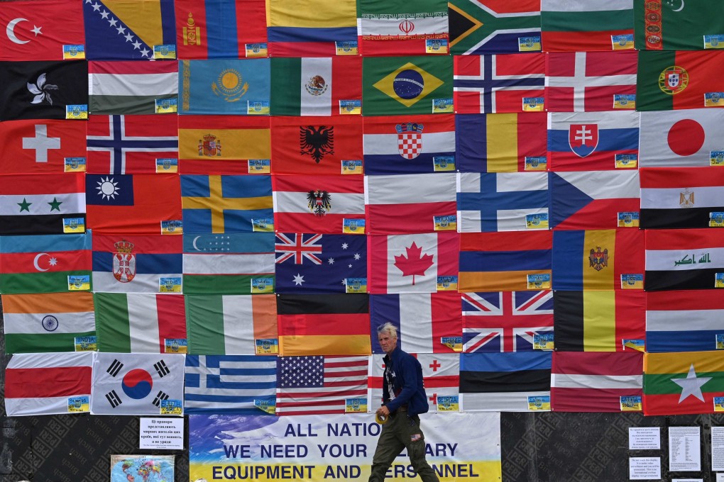 A man walks past a wall of flags next to a placard reading: “All nations, we need your military equipment and personnel please” on Independence Square in Kyiv, Ukraine, on June 23, amid a war with Russia. Photo: AFP