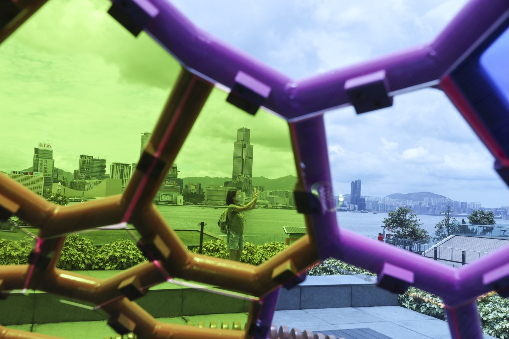 A woman taking a photo, flanked by the Tsim Sha Tsui skyline, is seen through an artwork set up in Tamar Park in Admiralty to celebrate the 25th anniversary of the establishment of the Hong Kong special administrative region, on June 22. Photo: Nora Tam