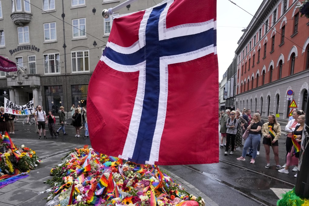A Norwegian national flag waves over flowers and rainbow flags placed at the scene of a shooting in central Oslo, Norway on Sunday. Photo: AP