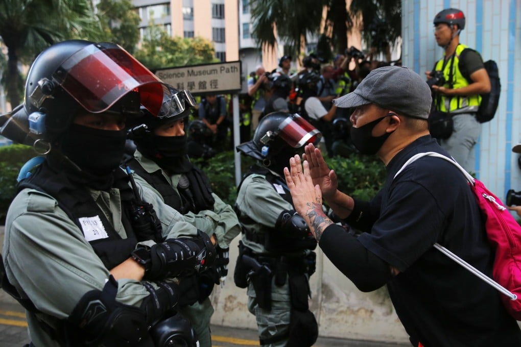 A supporter of pro-democracy protesters still holed up in Polytechnic University speaks to riot police officers patrolling the campus in Tsim Sha Tsui, Hong Kong on November 25, 2019. Photo: EPA-EFE
