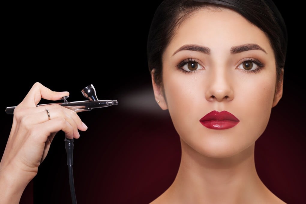 A model demonstrates an airbrush. The device sprays a fine mist of make-up onto your face for an exceptionally smooth, even finish that looks natural.