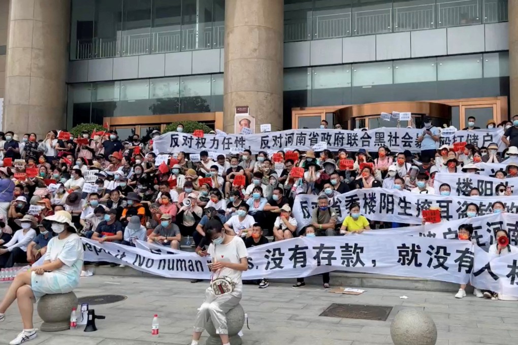 Demonstrators held banners during a protest over the freezing of deposits by rural-based banks, outside the Zhengzhou branch of the People’s Bank of China on July 10, 2022 in the Henan provincial capital, in this screengrab taken from video obtained by Reuters.