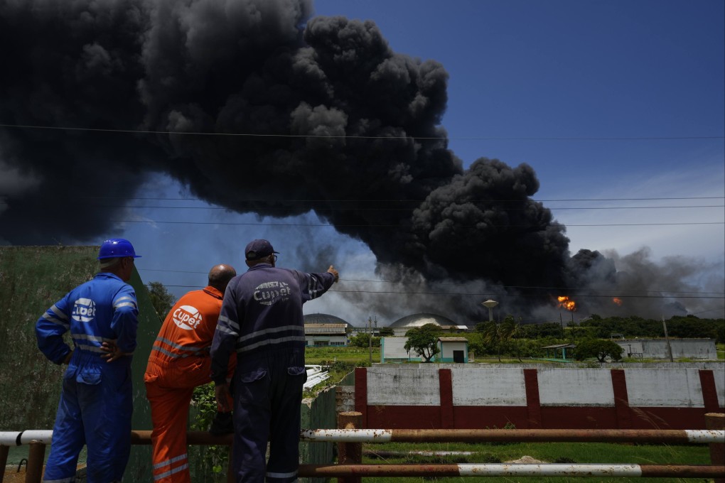 Workers of the Cuba Oil Union, known by the Spanish acronym CUPET, watch a huge rising plume of smoke from the Matanzas Supertanker Base, as firefighters work to quell a blaze which began during a thunderstorm the night before, in Matanzas.  Photo: AP