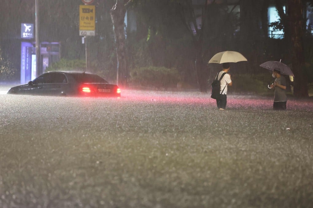 People wade alongside submerged cars in the Gangnam district of Seoul on Monday night. Photo: Yonhap/AFP