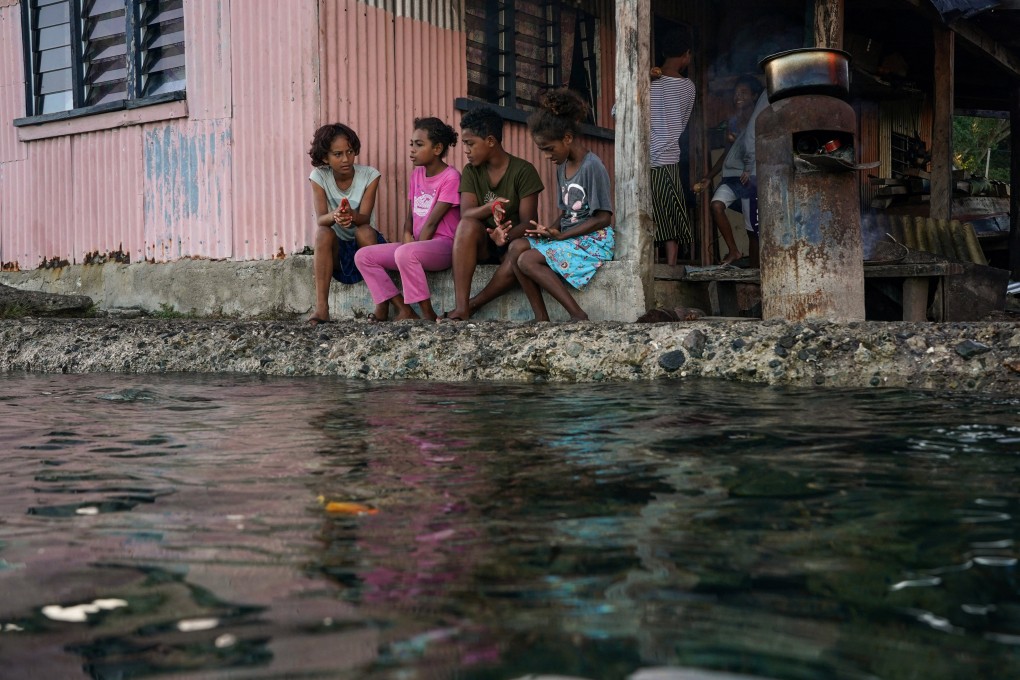 Children sit in front of a house next to a flooding sea wall in Fiji last month. Photo: Reuters