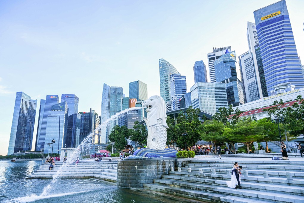 In this photograph taken on February 18, 2022, a couple poses for pre-wedding photographs next to the Merlion statue in Singapore. - Rivals Singapore and Hong Kong have become pandemic polar opposites, the former opting to live with the coronavirus and reopen to the world while the latter doubles down on zero-Covid and its international isolation. Photo: AFP