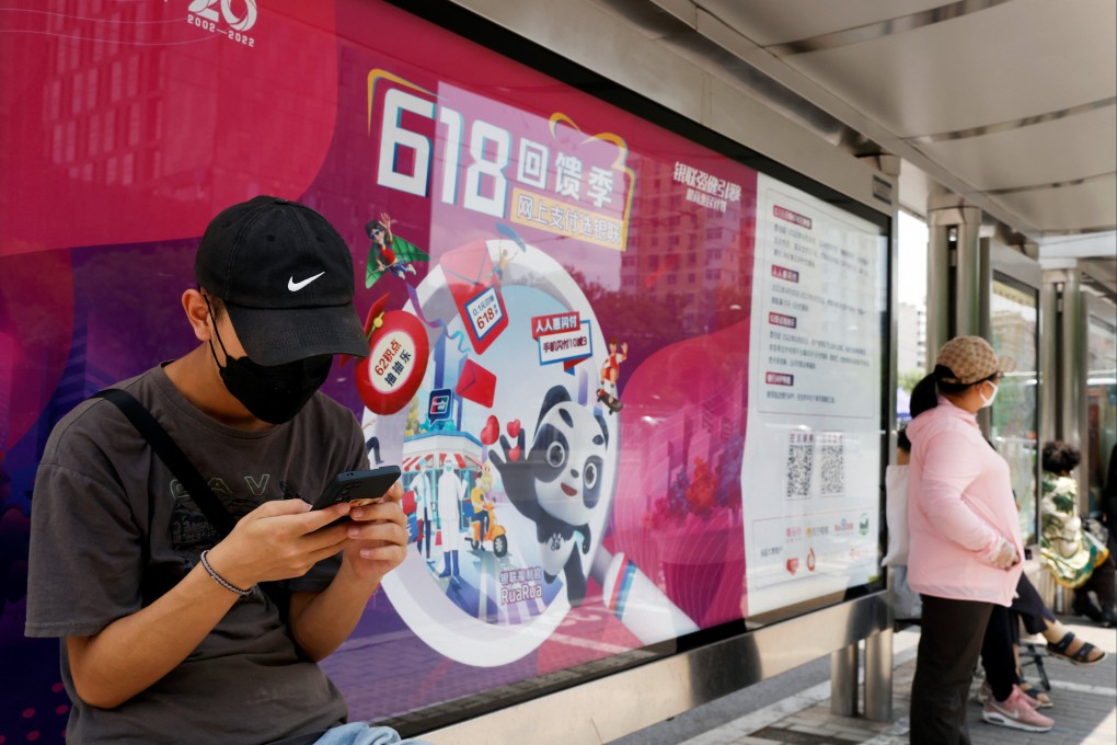 A man wearing a face mask uses his phone in front of a Unionpay advertisement for the “618” shopping festival at a bus stop in Beijing, June 14, 2022. Photo: Reuters