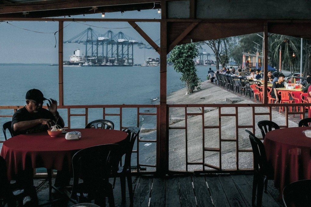 Customers sit in a restaurant with gantry cranes in the background at Port Klang, Selangor, Malaysia, on August 12. As countries reopen, intraregional trade in Asia could help offset the effects of economic slowdowns elsewhere. Photo: Bloomberg