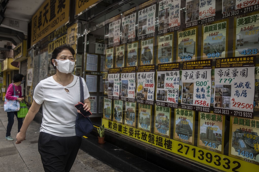 A woman walks past a real estate agent’s office in Hong Kong. Prices hit the lowest level since February 2020 in July. Photo: AFP