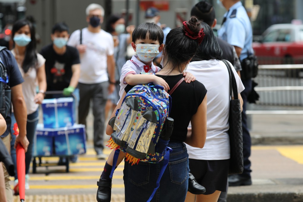 A child wearing a mask is carried by an adult as they cross the road in Central. If the vaccine pass scheme is expanded to include young children, it will impose a burden on low-income families having to buy smartphones for children. Photo: Nora Tam