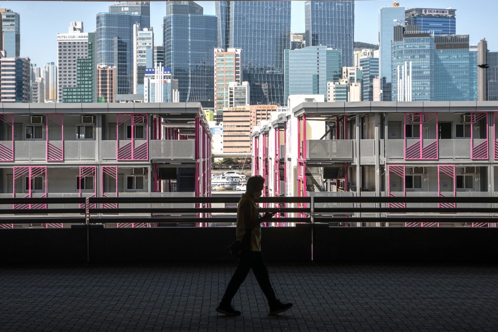 Skyscrapers can be seen behind an isolation facility in Kai Tak as a man passes in a mask, on June 28. Photo: Bloomberg