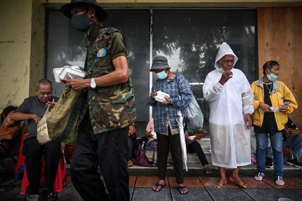 People shelter from the rain after receiving meals from volunteers from Bangkok Community Help Foundation in Bangkok on September 13. Soaring energy prices are driving inflation in economies like Thailand, where the energy-intensive transport category has a big weight in the consumption basket. Photo: AFP