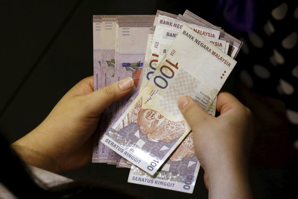 A woman counts her ringgit banknotes outside a money changer in Singapore. Barisan Nasional has promised cash aid to households with monthly incomes of less than 2,208 ringgit. Photo: Reuters