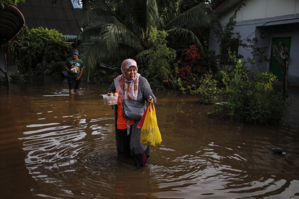 A woman holds eggs and food while walking through flood waters ahead of 15th General Election in Klang, state of Selangor, Malaysia on Saturday. Photo: EPA-EFE