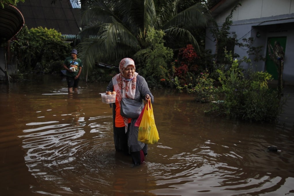 A woman holds eggs and food while walking through flood waters ahead of 15th General Election in Klang, state of Selangor, Malaysia on Saturday. Photo: EPA-EFE