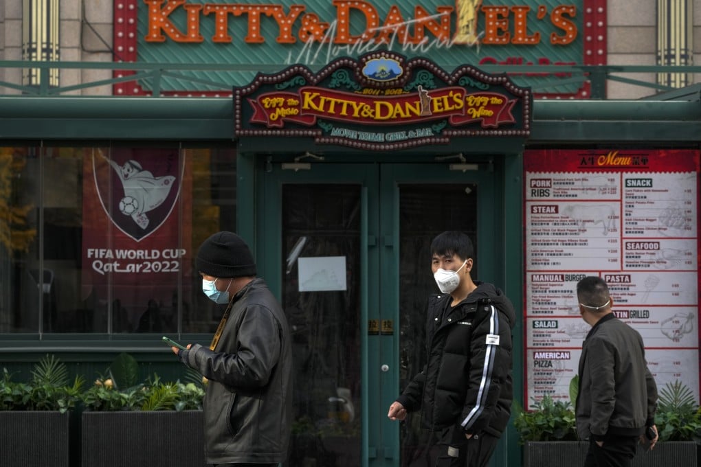 People wearing face masks walk by a closed restaurant displaying World Cup posters. Photo: AP