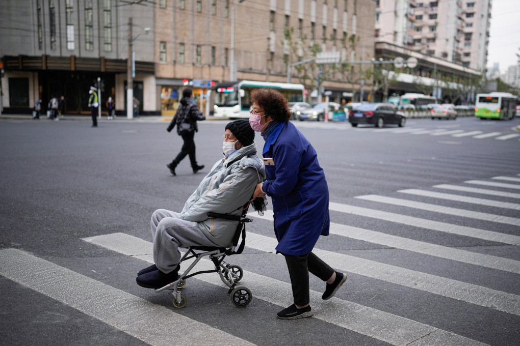 A woman pushes an old man in wheelchair to cross a street on Tuesday, as coronavirus outbreaks continue in Shanghai, China. Photo: Reuters