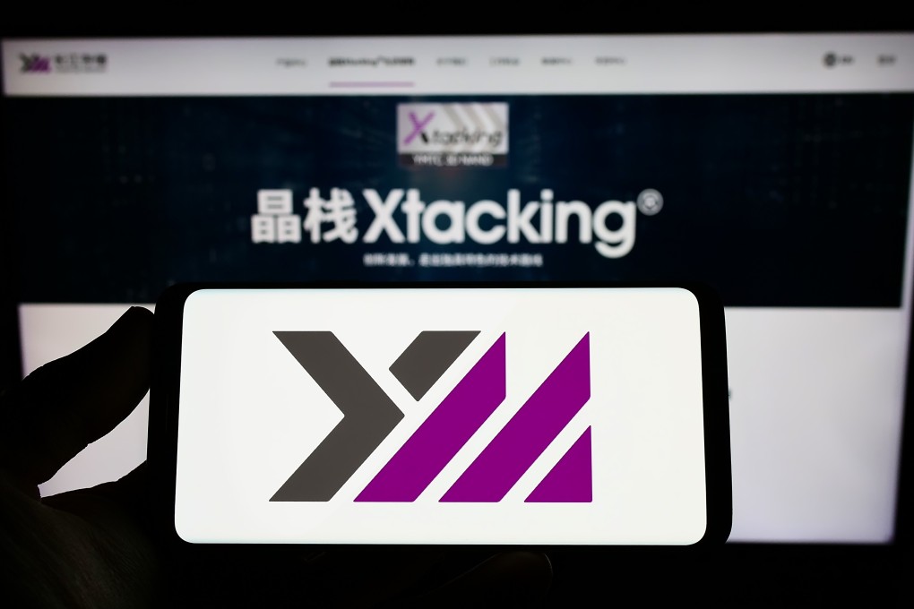 A smartphone showing the logo of YMTC is seen in front of a website detailing its Xtacking architecture. Photo: Shutterstock