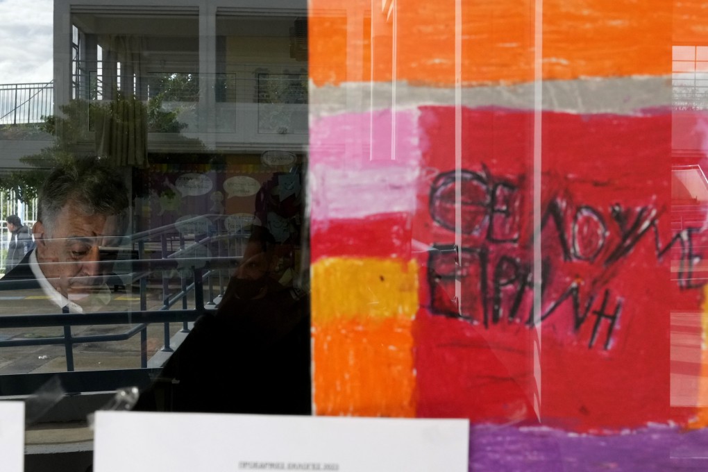 A painting on a classroom window reads “We need Peace” in Greek as a man casts his vote during the Cypriot presidential elections. Photo: AP