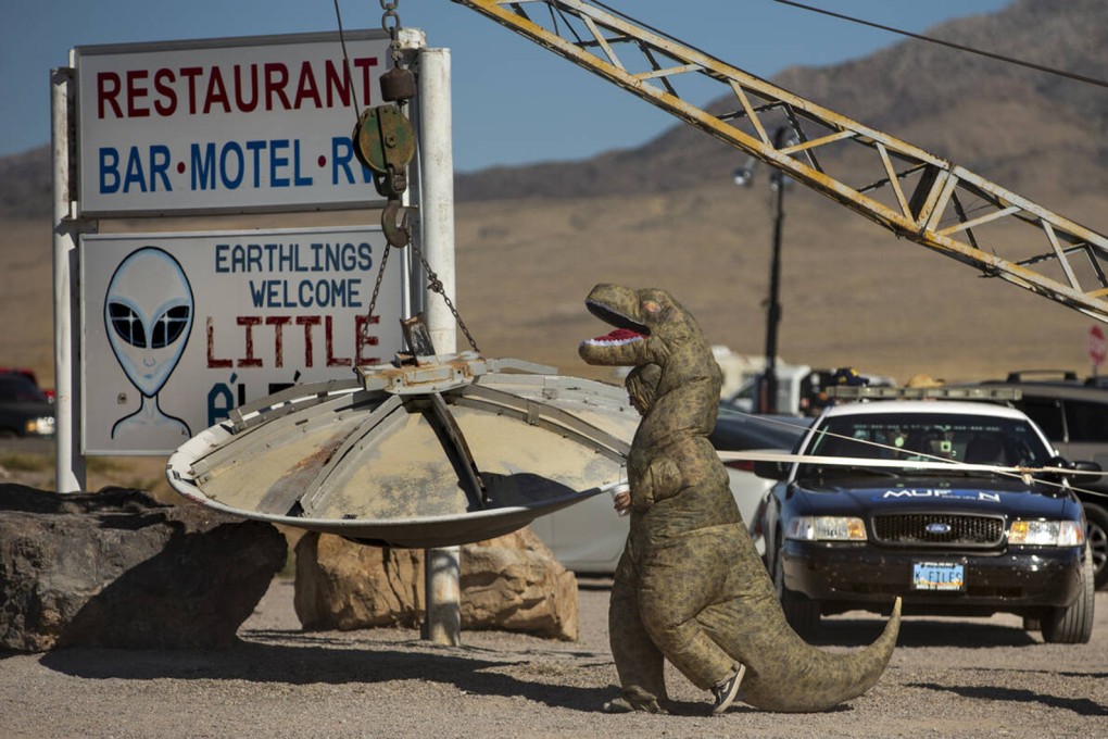 A person in a dinosaur costume walks over to the flying saucer outside the Little A’Le’Inn during the Alienstock festival in Rachel, Nevada, in September 2019. Photo: TNS