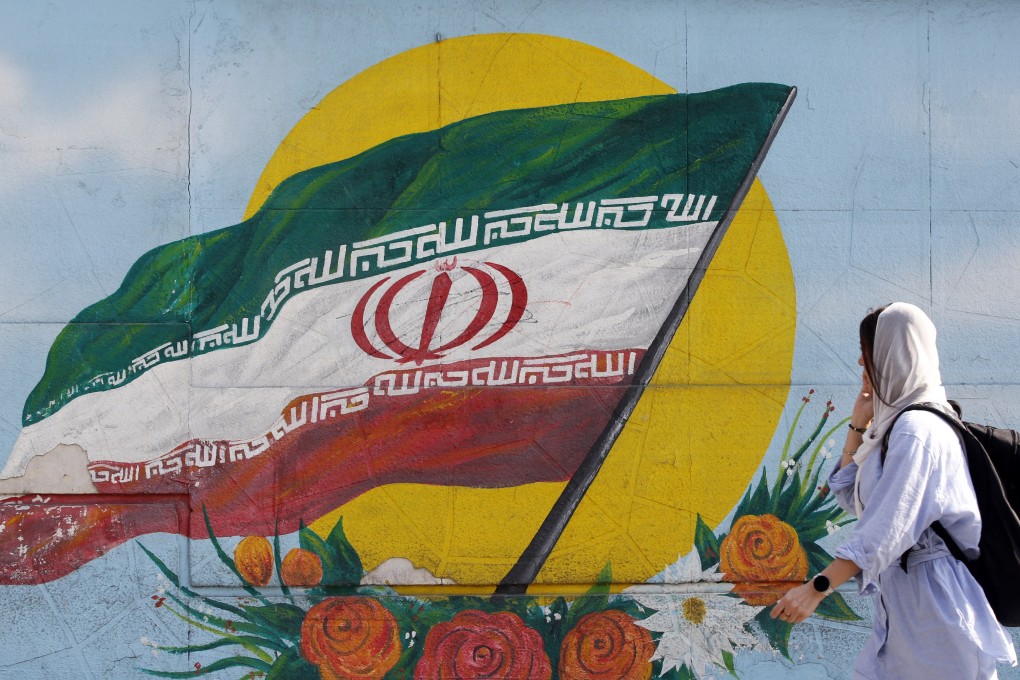 A woman wearing a headscarf walks past graffiti showing the Iranian national flag in Tehran, Iran. Photo: EPA-EFE