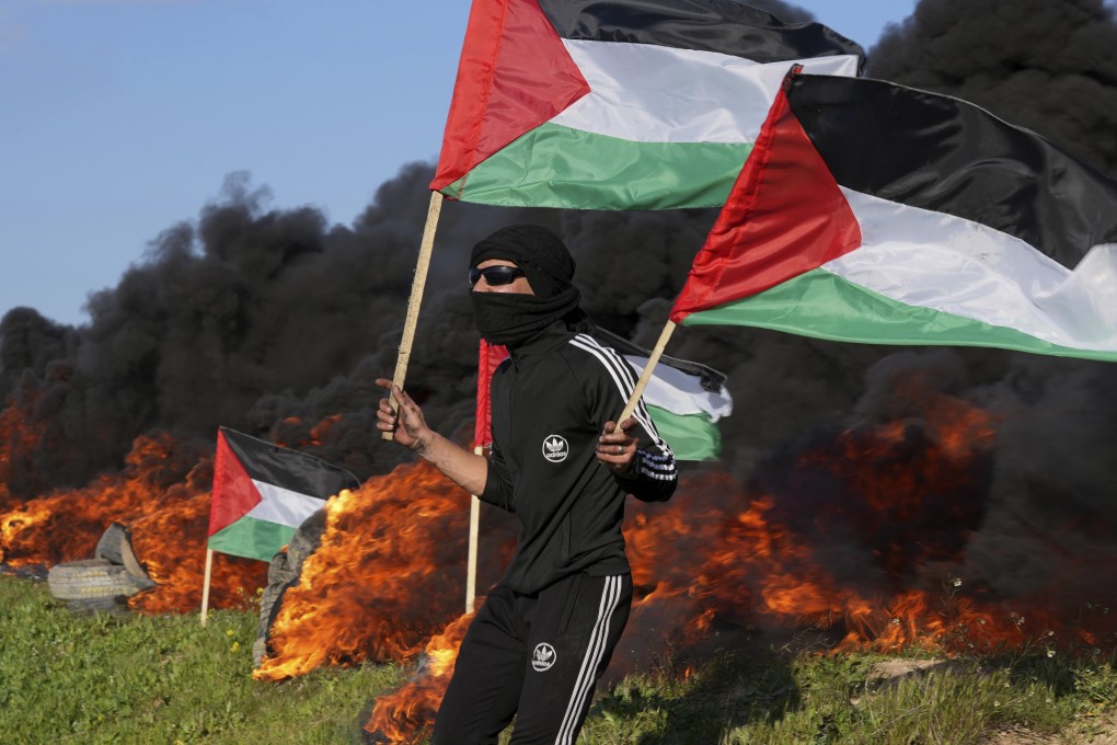 A demonstrator waves flags as others burn tyres during a protest against a deadly Israeli military raid in the West Bank city of Nablus on Wednesday. Photo: AP