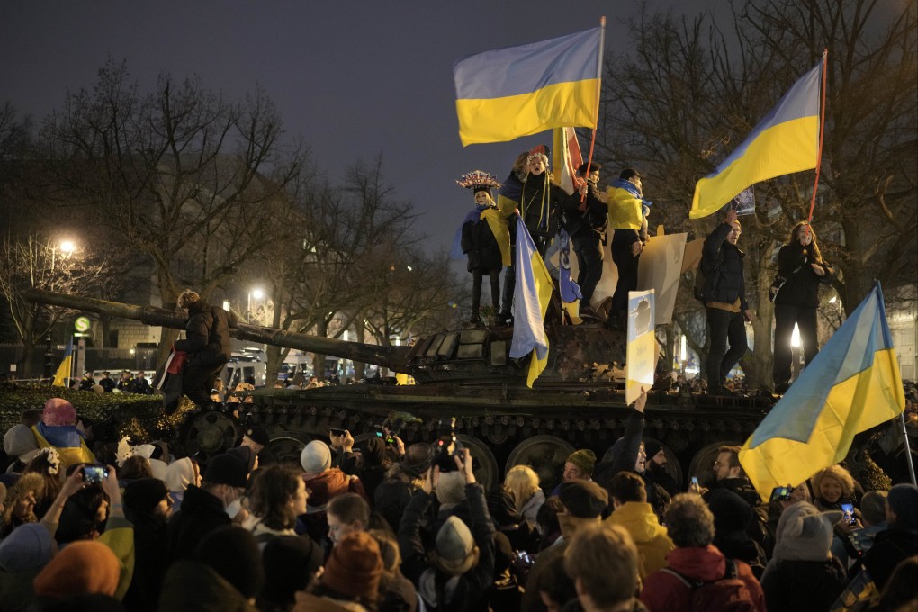 People wave Ukrainian flags as they stand on top of a wreck of a Russian T-72 tank, destroyed on the approach to Kyiv and placed in front of the Russian Embassy in Berlin on Friday. Photo: AP