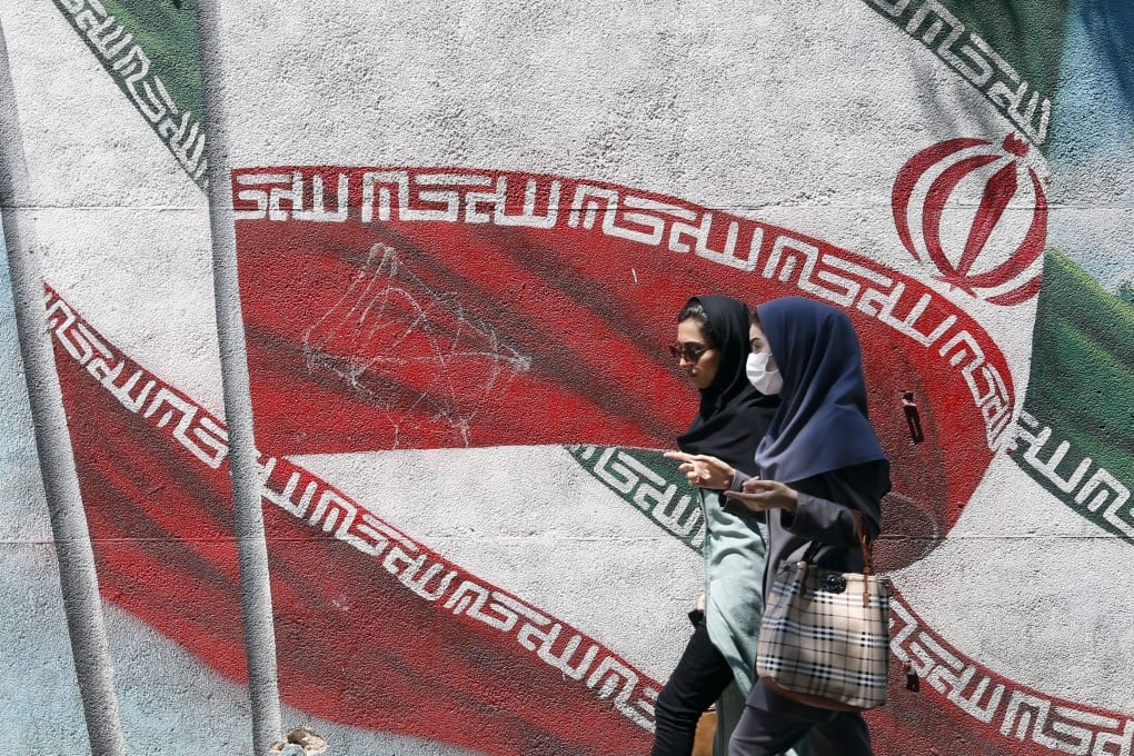 Young Iranians walk past a painting of Iran’s national flag in a street in Tehran. There are reports some schoolgirls are being poisoned to prevent them learning. File photo: EPA-EFE