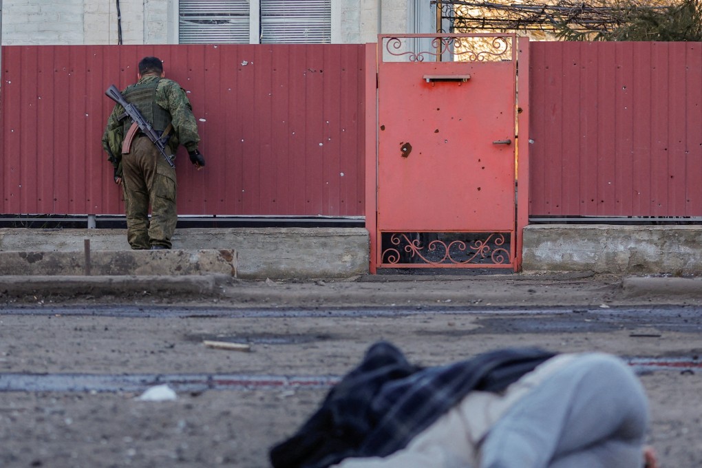 A soldier looks through a hole in a fence near the body of a woman killed by shelling in Ukraine. Photo: Reuters