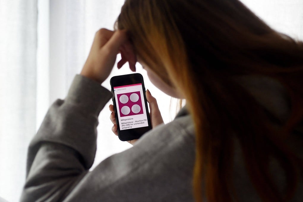 A woman looks at a website with the mifepristone abortion pill on her phone. Photo illustration: AFP