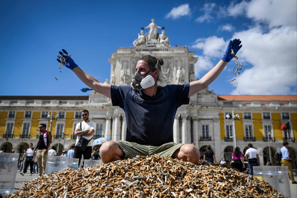 A German environmental activist throws cigarette butts as he sits on top of a pile of them, collected in one week, at Comercio square in Lisbon, Portugal on Sunday. Photo: AFP